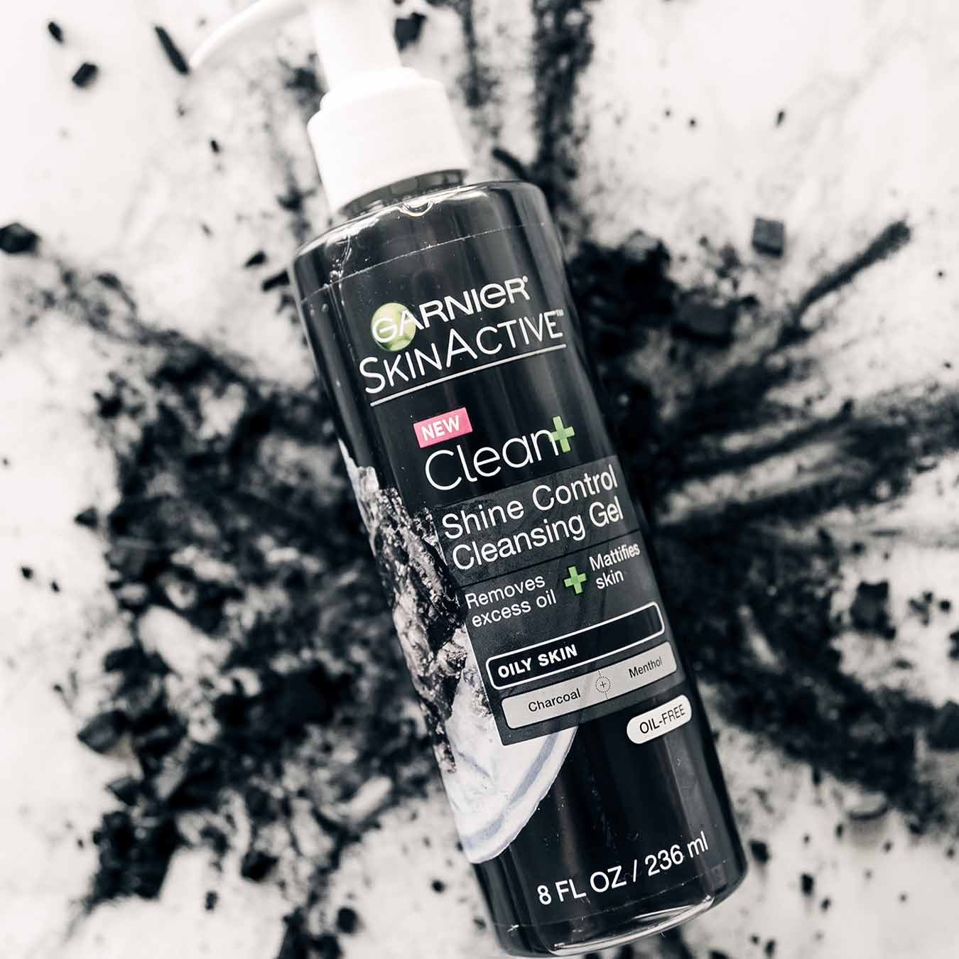 Garnier SkinActive Clean+ Shine Control Cleansing Gel floating above an explosion of charcoal powder on white marble.